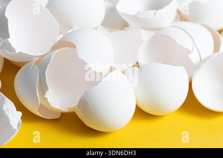 Eggshells are lying on a yellow surface, showing fragments and cracks. The scene highlights the remnants after cooking or baking. Stock Photo