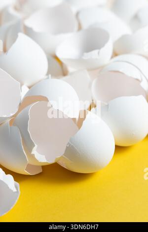 A collection of broken eggshells lies on a bright yellow surface. The pieces show the inner texture and color as they are spread out randomly. Stock Photo