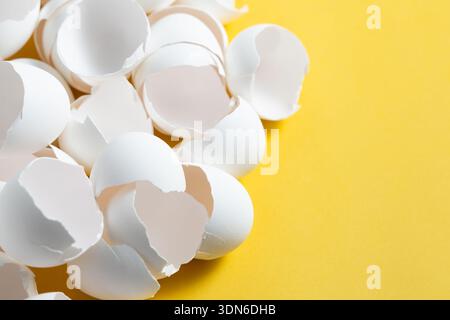 White eggshells are scattered on a bright yellow surface. They are broken and empty, suggesting that eggs were used for cooking. Stock Photo