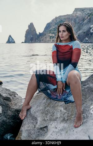 Woman Seascape Beach Fashion - A woman in a colorful dress sits on a rock overlooking the sea. Stock Photo
