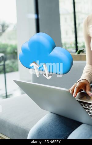 Cloud storage symbol appears above a person using a laptop at home during the day Stock Photo