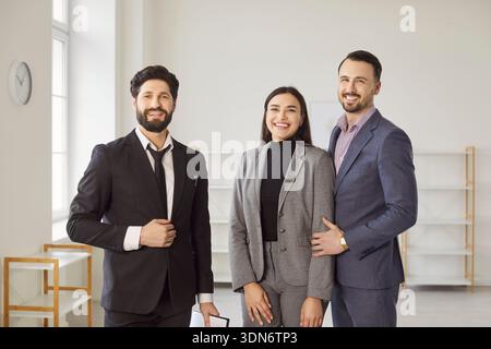 Young man realtor standing with happy couple looking at camera in new house. Stock Photo