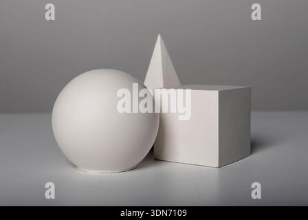 white geometric shapes including a sphere, cube, and pyramid arranged on a neutral surface. Clean abstract still life with matte textures, soft shadow Stock Photo