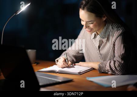 Happy freelance worker scheduling in paper agenda working in the night Stock Photo