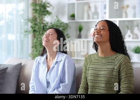 Happy diverse women sitting on a couch at home breathing fresh air together Stock Photo