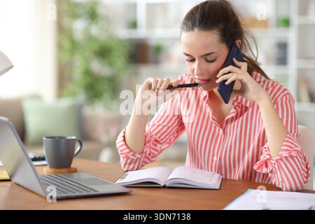 Self employed working at home talking on phone and consulting paper agenda Stock Photo