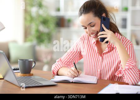 Happy tele worker talking on phone and scheduling in agenda working at home Stock Photo