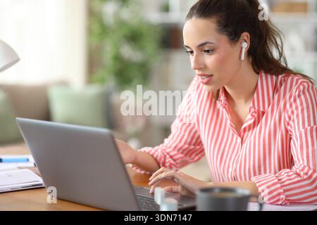 Tele worker wearing earbuds talking during a video call using laptop working at home Stock Photo