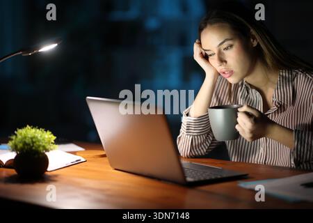 Tired freelance worker overworking drinking coffee in the night at home Stock Photo