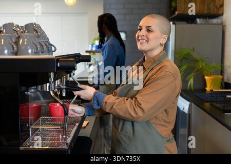 Diverse baristas smiling and operating espresso machine behind coffee shop counter with red cups Stock Photo