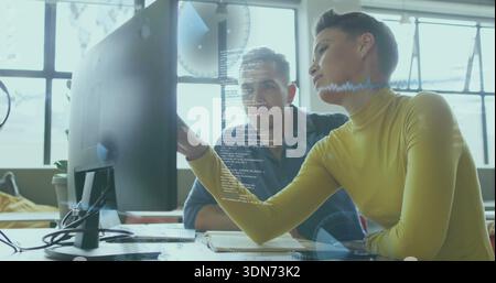 Pointing tech lead wearing mustard top guiding coworker in dark shirt at office with wide monitor Stock Photo