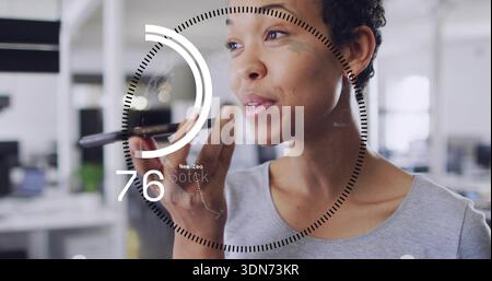 Speaking woman wearing light grey top, holding slim black device in modern office, HUD overlay Stock Photo