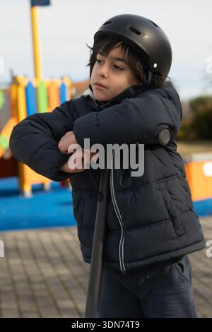 Boy wearing a helmet and winter jacket, standing outdoors, looking thoughtful Stock Photo