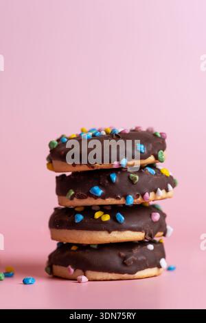 This image showcases a stack of delectable chocolate donuts topped with vibrant colorful sprinkles, creating an eye-catching and appetizing visual del Stock Photo
