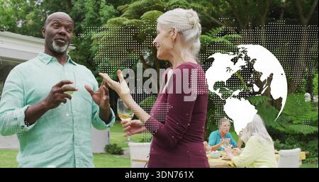 Talking couple in green and burgundy holding wine glasses at patio table in backyard, globe overlay Stock Photo