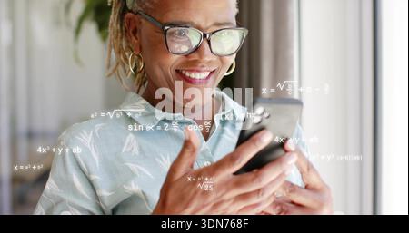 Smiling woman in blue blouse with glasses and hoops holding phone at window, seeing math overlays Stock Photo