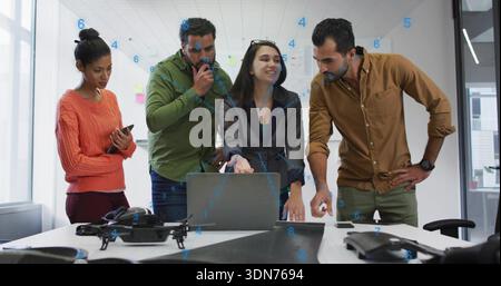 Discussing four staff in workwear at office examining drone parts with open laptop and smartphone Stock Photo