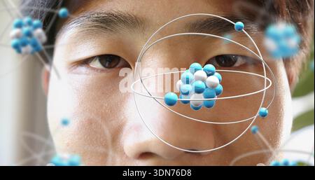 Framing mid adult Asian male face inside room, showing AR molecular model orbiting right eye Stock Photo