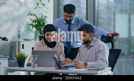 Three Arabian colleagues Muslim co-workers Hindu business team with computer Indian partners managers businesspeople in office working together Stock Photo