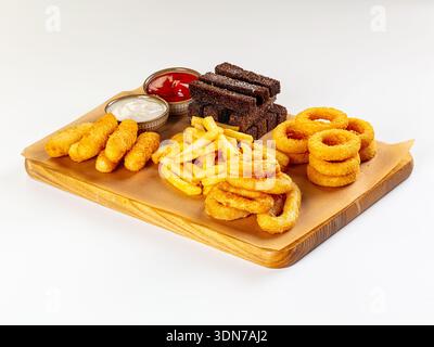 Assorted fried snacks on a wooden board, isolated on white. Golden onion rings, fries, cheese sticks, and rye croutons with ketchup and white sauce. P Stock Photo