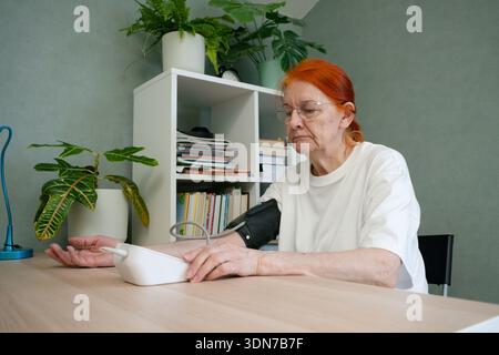 Side view of a senior woman with a sad, concerned expression as she checks her blood pressure. Focus on profile and health worry. Stock Photo
