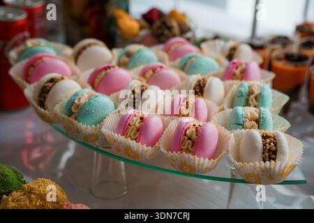 A vibrant assortment of pastel-colored macarons in decorative paper cups arranged on a glass stand, showcasing delicate textures and creamy fillings i Stock Photo