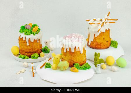 Easter cakes with white frosting, moss decoration and quail eggs on white plates. Festive spring composition with colorful bunnies and edible willow b Stock Photo