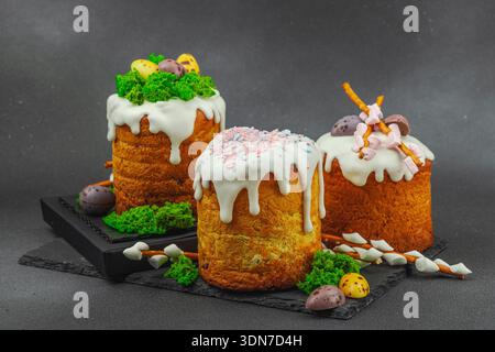 Easter cakes decorated with edible moss nest, chocolate eggs and handmade willow branches. Traditional festive dessert with bunny figures on black sto Stock Photo