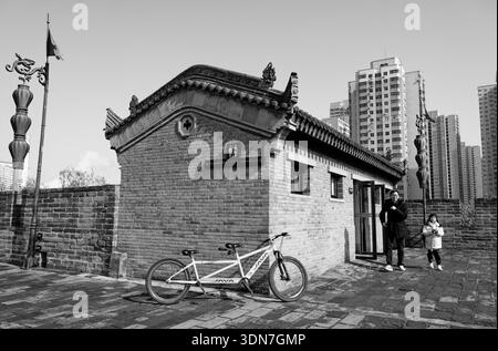 Tandem bicycle rests by a small brick pavilion as winter life moves on the ancient city wall of Xi'an Stock Photo