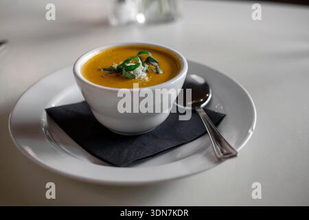 Cup of yellow soup on saucer with a spoon Stock Photo