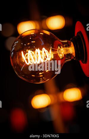 A close-up view of a glowing filament bulb emitting warm light, with soft bokeh highlights in the background. Stock Photo