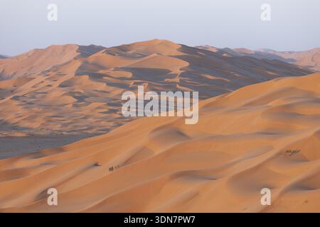 Aerial view of golden dunes cascading under a soft, pale sky, creating a mesmerizing contrast of warm and cool tones, Salalah, Al Wusta Governorate, O Stock Photo
