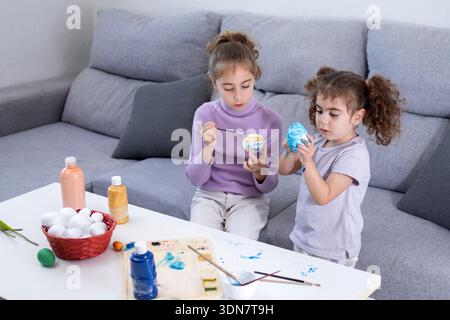 Two sisters decorating Easter eggs at home Stock Photo
