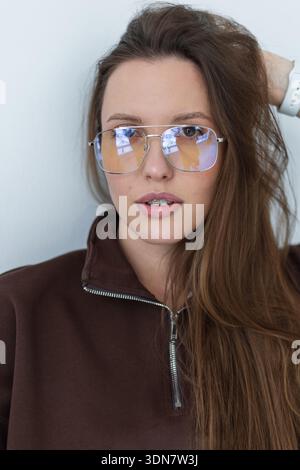 High-quality shot of silver metal aviator glasses on a model. Detail of the blue light lens reflection and frame design. Clean composition with brown Stock Photo
