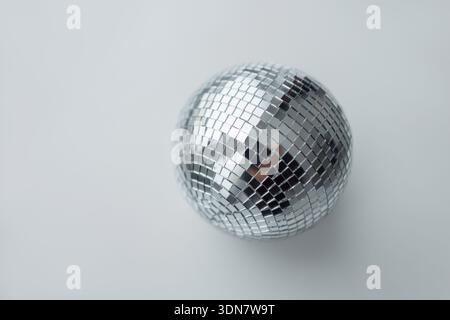 Top view of a glittering silver disco ball centered on a clean, neutral grey background. High-quality studio shot highlighting reflective mirror tiles Stock Photo