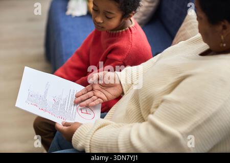 Black woman showing graded school paper with large red F to Black child sitting beside her, child looking down with disappointed expression, adult holding document in hand Stock Photo