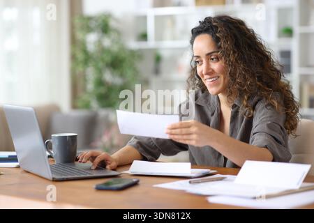 Happy freelancer checking bills and doing online accounting with a laptop working at home Stock Photo