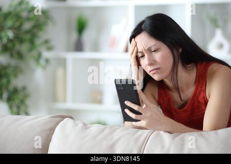 Worried asian woman checking online content on phone at home Stock Photo