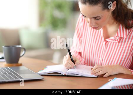 Serious tele worker writing in agenda working at home Stock Photo