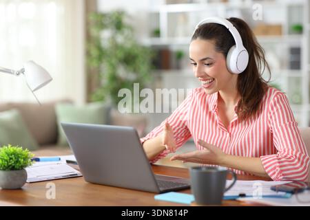 Happy freelance worker wearing headphone talking during a video call using laptop at home Stock Photo