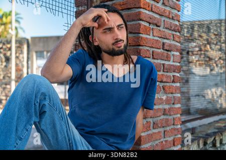 Young man with dreadlocks, serious and thoughtful, sitting outdoors in summer. Stock Photo