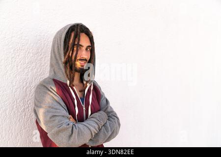 Young man with dreadlocks stands confidently against a white wall Stock Photo