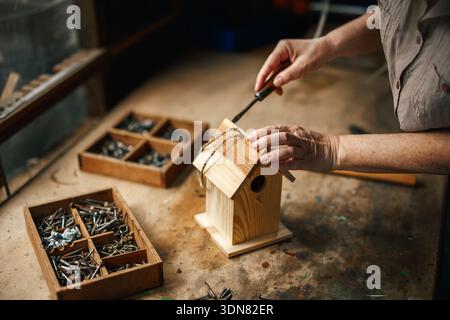 Woman making homemade wooden birdhouse in workshop. Work tools on table Stock Photo