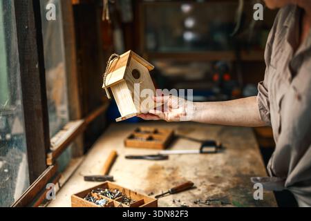 Woman making homemade wooden birdhouse in workshop. Work tools on table Stock Photo