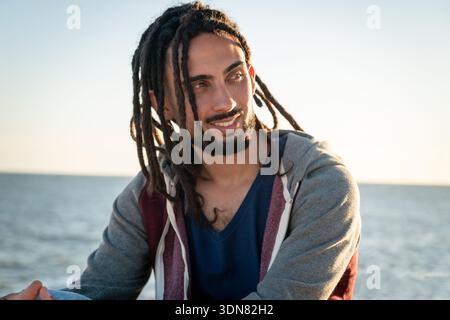 Smiling young man contemplating the view of the ocean at sunset Stock Photo