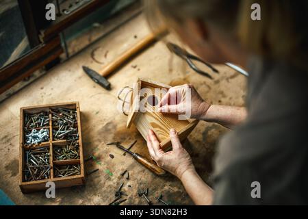 Woman crafting homemade wooden birdhouse in workshop. Work tools on table Stock Photo