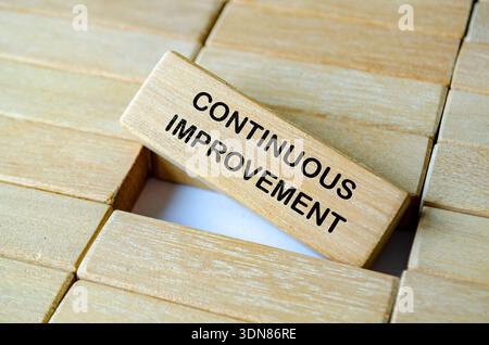 CONTINUOUS IMPROVEMENT text on wooden blocks with ladder representing step by step enhancement and organizational development. Stock Photo