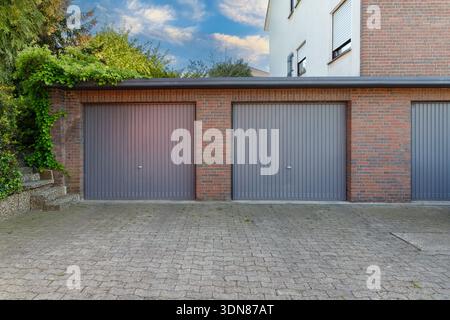 Modern parking garage in residential brick house for cars with grey roller shutters on gates. Closed doors in garages. Stock Photo