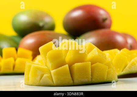 Juicy mango cubes with whole fruits on yellow background Stock Photo