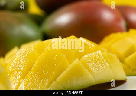 Juicy mango cubes with whole fruits on yellow background Stock Photo